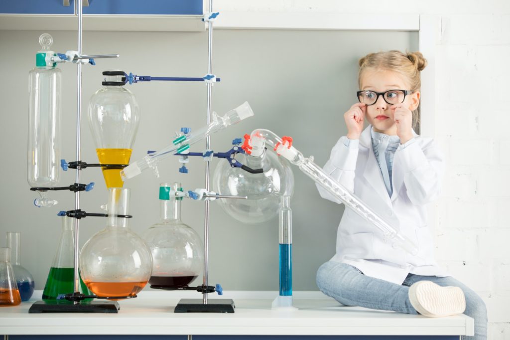 Little girl in white coat and eyeglasses sitting on table in science laboratory